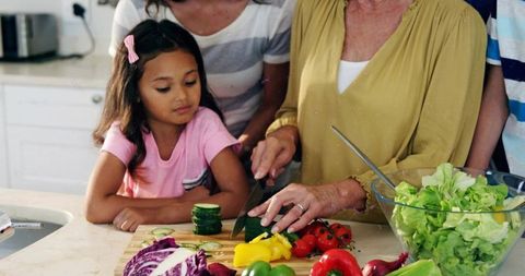 Multigenerational family preparing salad, grandmother teaching child slicing vegetables