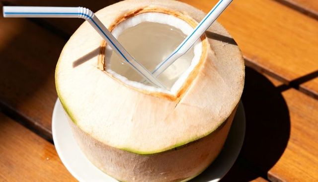 Tropical young coconut drinking water with straws on sunlit wooden table closeup