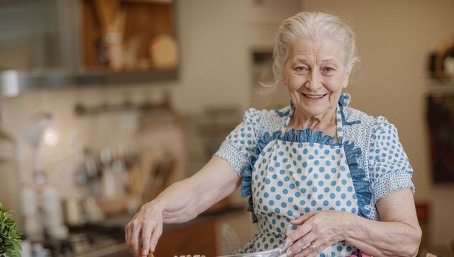 Senior woman baking at home smiling while stirring batter in polka dot apron