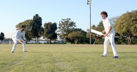 Two Cricket Players Batting and Fielding on Sunny Grass Oval During Golden Hour Match