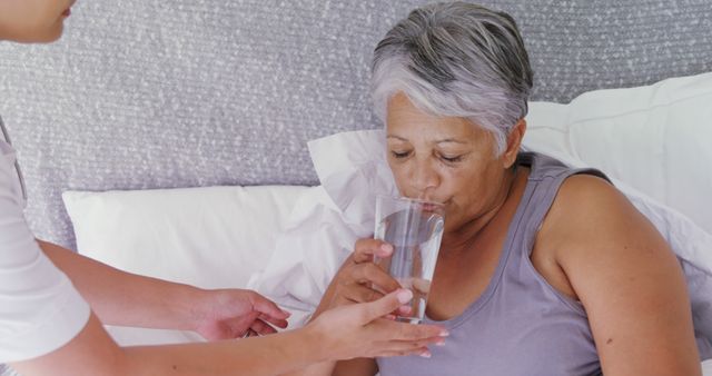 A middle-aged woman is being assisted with drinking water by a caregiver, with copy space. The scene underscores the importance of care and support for individuals who may be unwell or need assistance with daily activities.