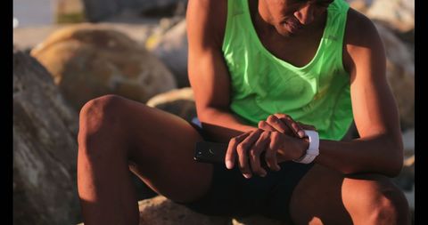 Athlete Wearing Smartwatch Relaxing on Rocks by Ocean - Download Free Stock Images Pikwizard.com