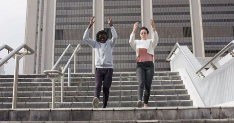 Diverse friends descending city stairs with raised arms showing movement and urban energy