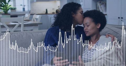 Couple sharing tender kiss on couch while holding phone with waveform overlay