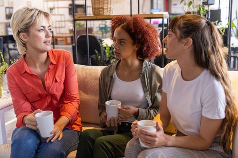 Diverse female coworkers networking in office lounge with coffee