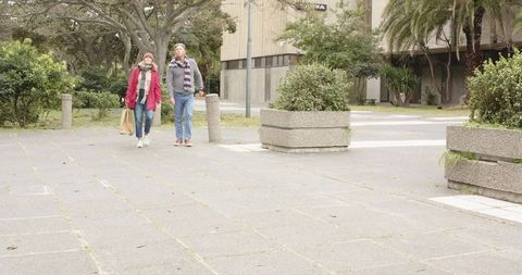 Middle-aged couple walking in urban plaza wearing scarves carrying brown paper bag