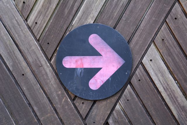 Bright neon arrow pointing right on a dark circular background on a wooden plank wall. Ideal for adding direction, emphasis on guidance, or navigation cues in social media posts, websites, advertisements, or presentation slides.