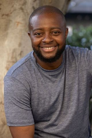 Smiling african man leaning on tree outdoor headshot for lifestyle wellness branding
