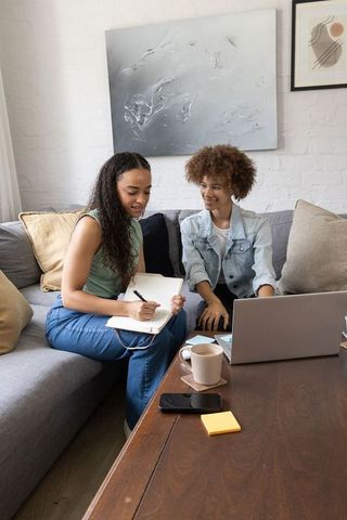 African female friends collaborating on home office project with laptop and notes