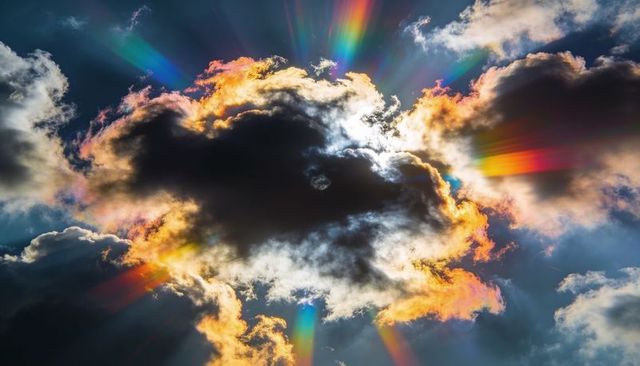 Dramatic backlit cumulus cloud casting rainbow sunbeams with iridescent cloud edges