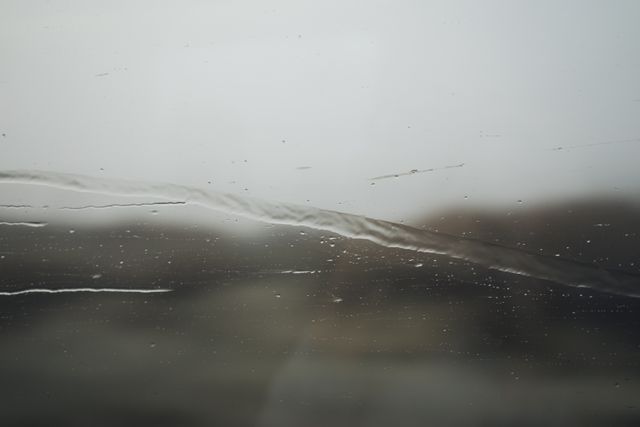 Raindrops visible on glass window with blurred outside background creates a melancholic and atmospheric mood. Great for themes of weather, autumn, and melancholy, can be used in blogs, websites, and presentations focusing on nature or reflective moods.