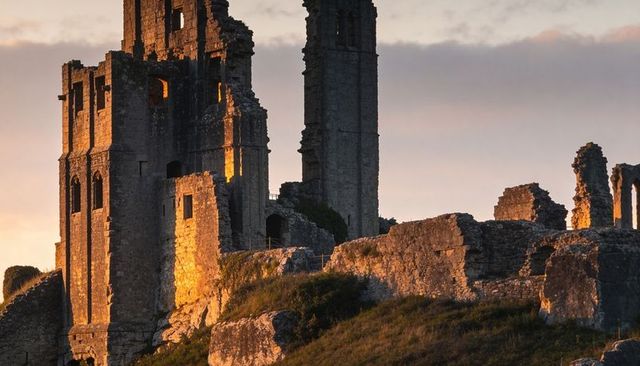 Golden-hour ruins of hilltop stone castle towering over grassy slope with arches