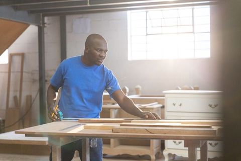 African American Carpenter Measuring Wood Plank with Tape Measure and Pencil