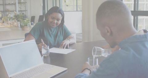 African american coworkers collaborating at office table signing document and pouring water