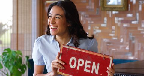 Smiling woman holding open sign in quaint cafe setting