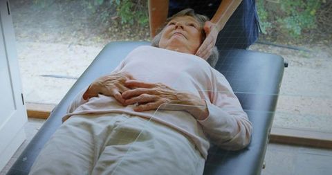 Elderly woman receiving gentle neck support during physiotherapy session on clinic table