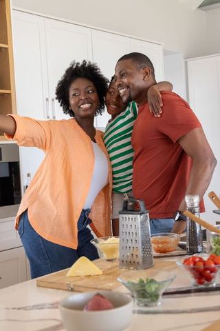 African american family taking selfie in bright kitchen while cooking together and smiling