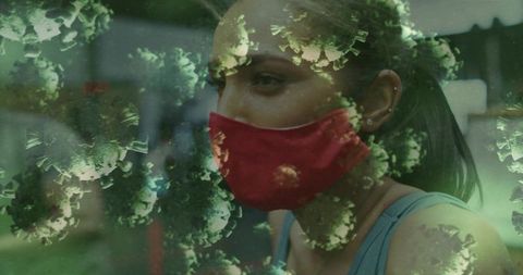 Young woman wearing red cloth mask amid green coronavirus overlay, contemplative portrait