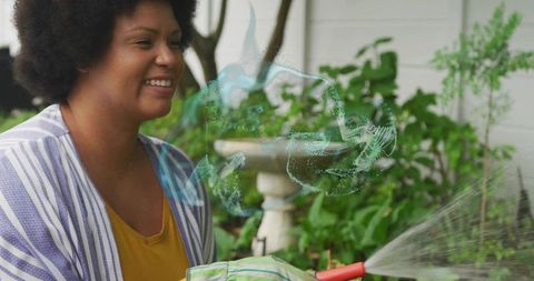 Smiling woman watering backyard garden with hose near decorative birdbath