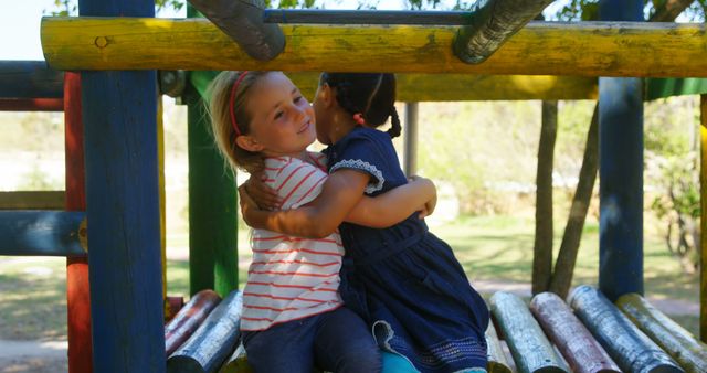 Two young girls hugging on colorful playground equipment, showcasing friendship and bonding in an outdoor setting. Great for themes of childhood, happiness, outdoor activities, and playtime during summer. Perfect for educational materials, parenting articles, and children's activity guides.