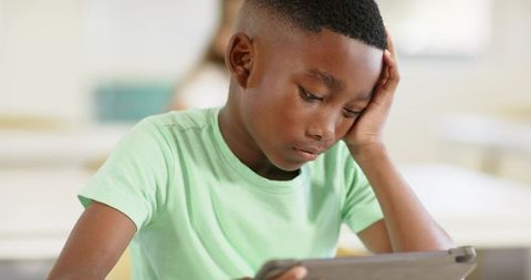 African american boy using tablet in classroom looking focused and thoughtful