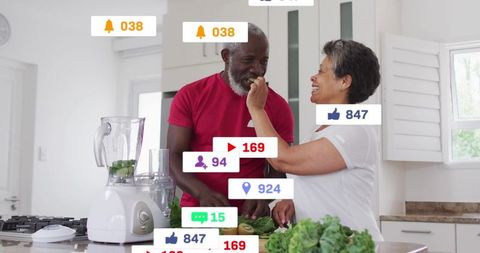 Mature couple preparing green smoothie and feeding partner fresh greens in bright kitchen