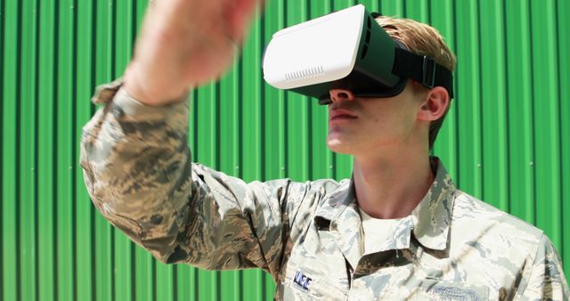 This image depicts a military personnel wearing a virtual reality headset for training purposes. The setting emphasizes modern technology and immersive learning techniques being integrated into military practices. Ideal for articles or presentations on advancements in military training, use of VR in various fields, and modern technology in defense.