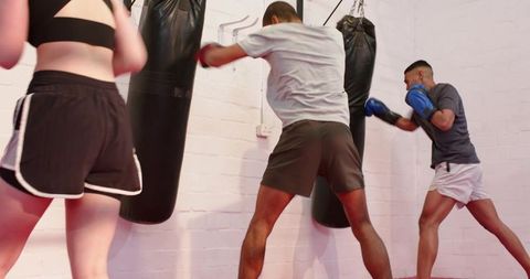 Multicultural group training boxing punching heavy bags at rotating stations in gym fitness class