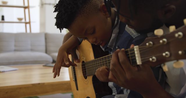 Father teaching son to play acoustic guitar in cozy living room. Great for family bonding, music education, and parenting themes. Suitable for promoting music lessons, family activities, or cozy home environments.