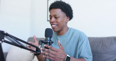 Young man recording podcast at home speaking into microphone and gesturing naturally