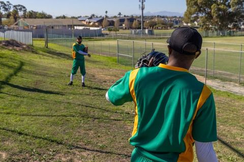 Two baseball players practicing throws and catching on sunny community field