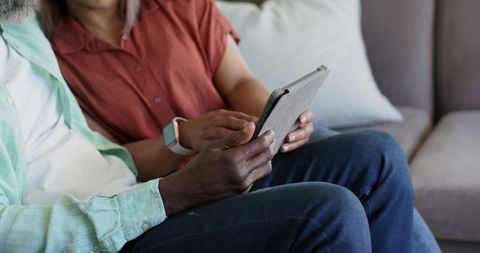 Diverse couple on sofa sharing tablet tapping screen embracing digital connection