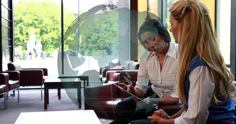 Women collaborating over tablet in modern lounge with globe reflection and copy space