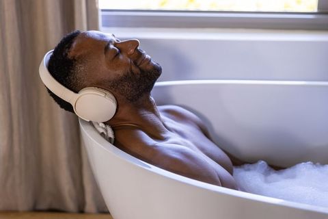 African man relaxing in bubble bath wearing headphones listening to music