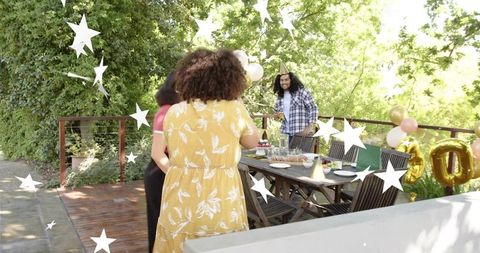 Friends celebrating outdoor birthday brunch on sunny deck with cake and balloons