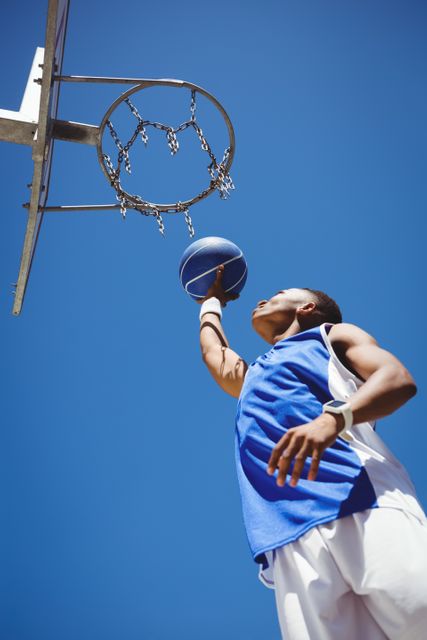 Low angle view of teenager playing basketball against clear blue sky