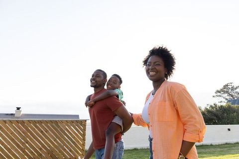 African american family walking on sunny lawn with father carrying child piggyback