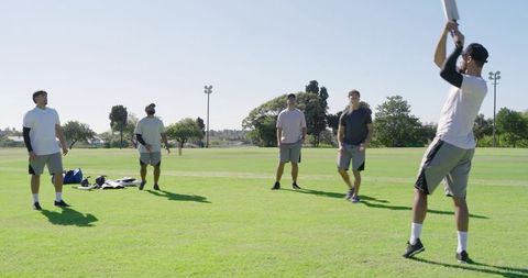 Diverse male teammates practicing cricket in suburban park during sunny training session