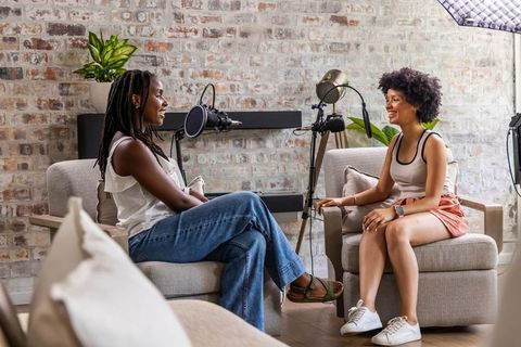 Two african american women recording casual podcast conversation in cozy loft studio