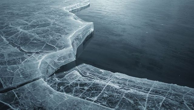 Fractured ice shelf splitting over dark open water with intricate surface crack network