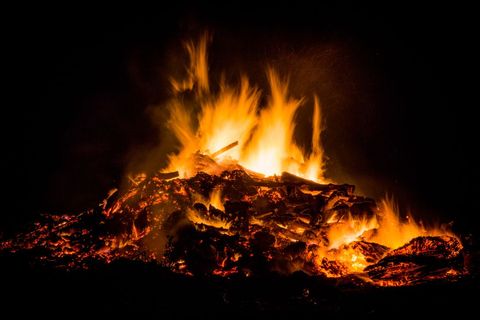 Intense night bonfire burning with glowing embers and towering flames against dark sky