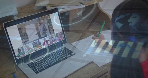 Girl writing while joining virtual classroom on laptop with hud overlay and study materials