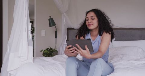 African american woman relaxing on bed using tablet in minimal neutral bedroom