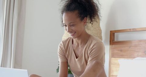 Smiling Woman Using Laptop in Cozy Bedroom Setting
