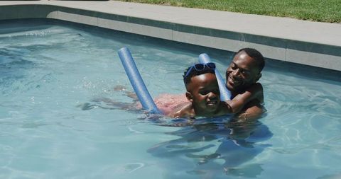 African american father and son playing in backyard pool with blue noodle and goggles