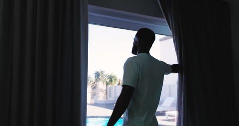 African American Man Standing at Sliding Glass Door Looking Out over Pool and Palms