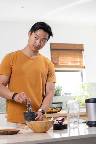 Asian man preparing fresh herb paste using mortar and pestle in bright modern kitchen
