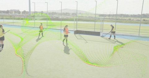 Female field hockey players training on artificial turf near goal with sticks