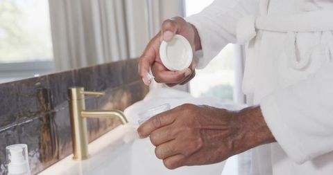 African-american mature man applying facial cream in minimalist bathroom morning routine