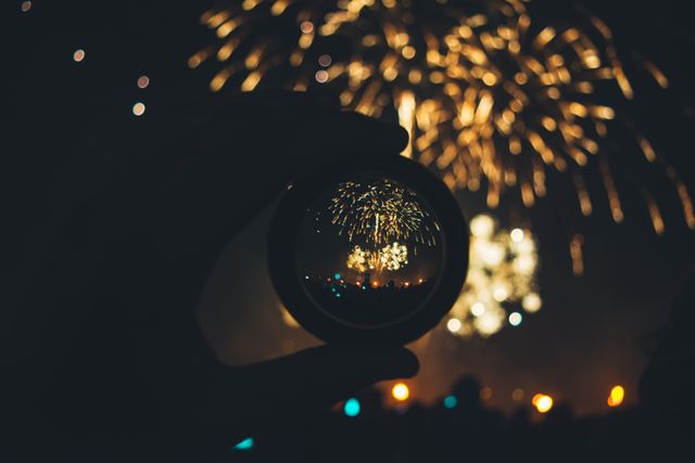 Hand holding magnifying glass reflecting colorful fireworks exploding in night sky. Ideal for festive celebration promotions, New Year Eve event advertising, festival posters, party invitations, and holiday-themed marketing.